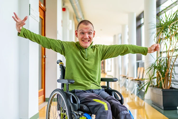 Happy Wheelchair User – Independent Living and Assistive Technology Smiling wheelchair user spreading arms in a bright hallway representing confidence and independence through assistive technology