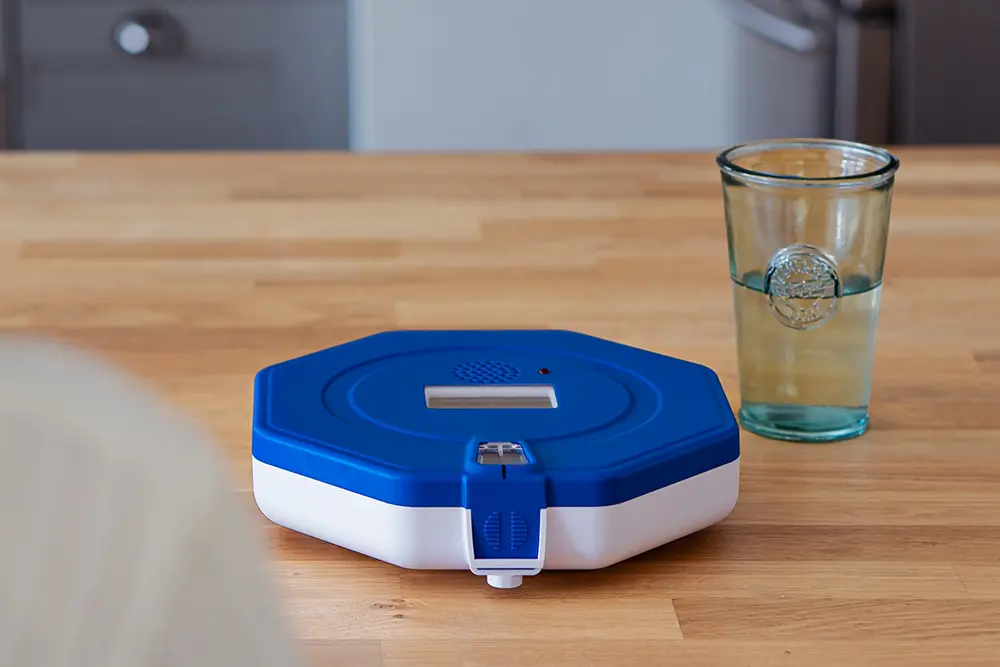 Automatic medication dispenser on a table beside a glass of water