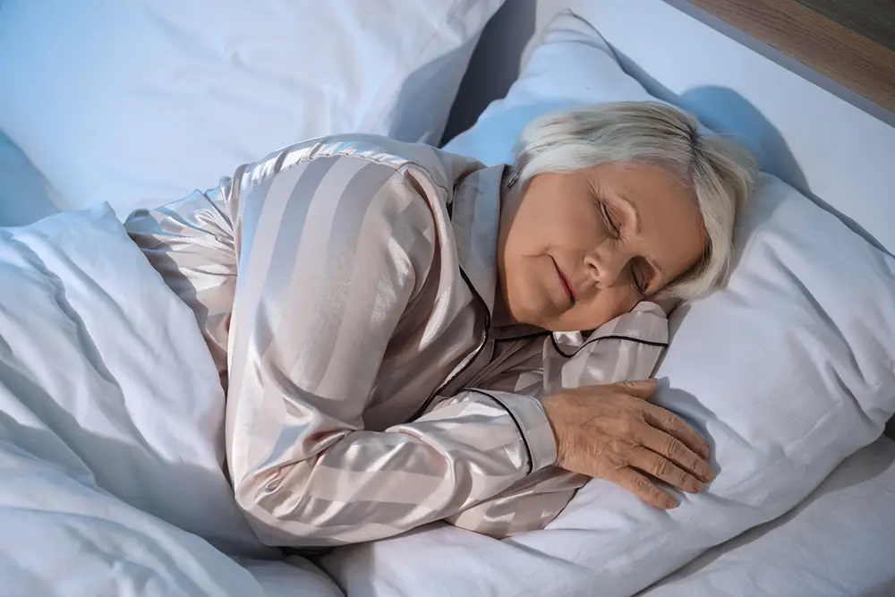 Person sleeping comfortably in bed demonstrating the discreet, ultra-thin BedSense sensor placed beneath bedding for unobtrusive overnight monitoring.