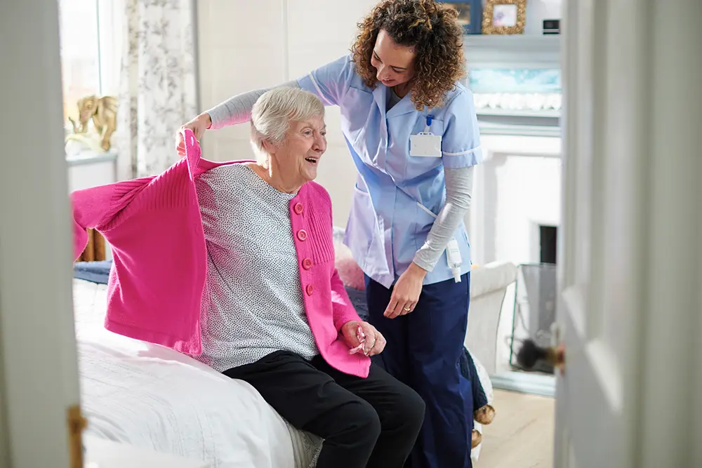Carer assisting an older person while BedSense reliably detects bed and chair occupancy to support safer care and timely assistance.