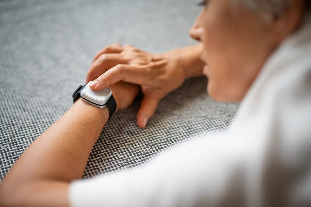 Person pressing the SOS button on a wrist-worn personal alarm to request assistance