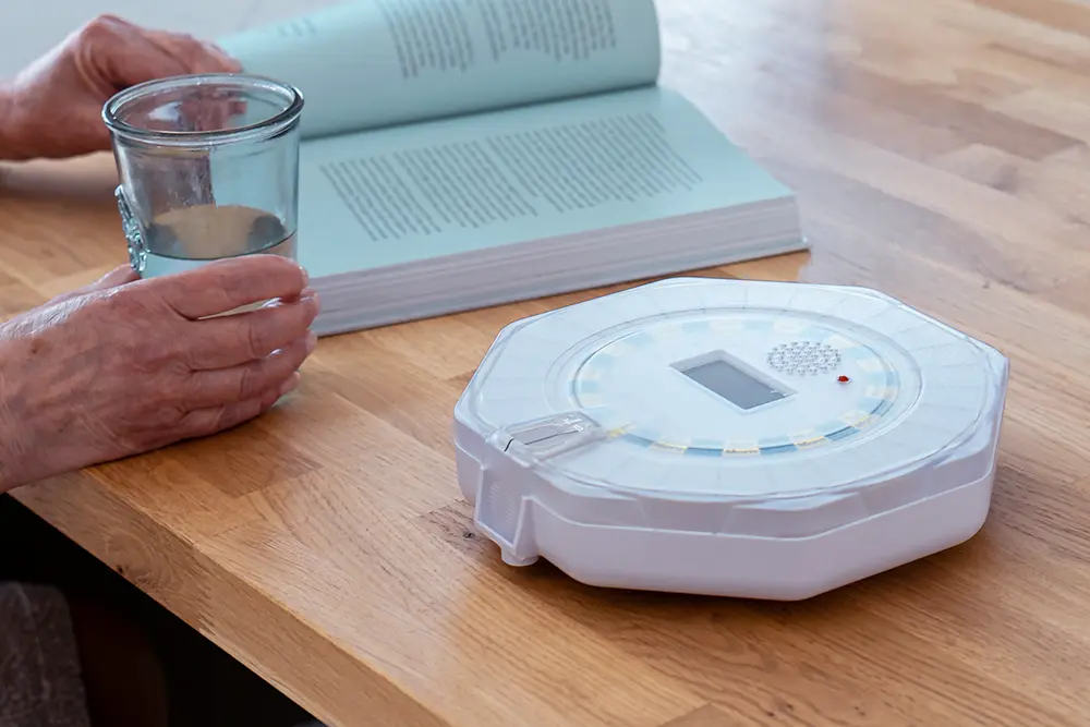 Lockable automatic medication dispenser on a table beside a glass of water