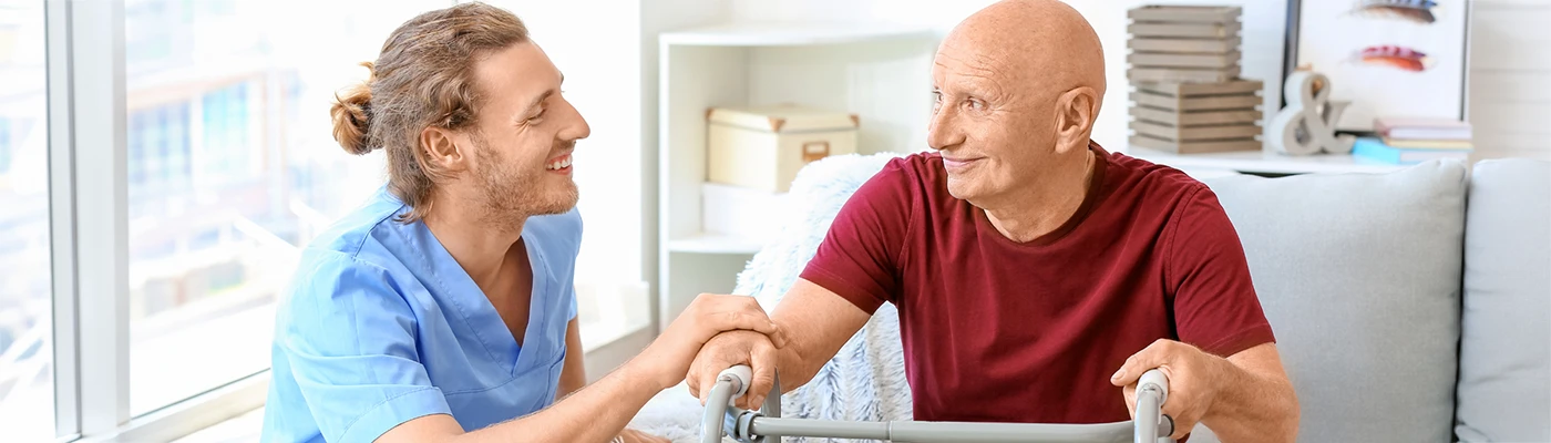 Falls Prevention and Early Intervention in Care Homes Care worker supporting an older adult using a walking frame as part of falls prevention and rehabilitation in a care setting.
