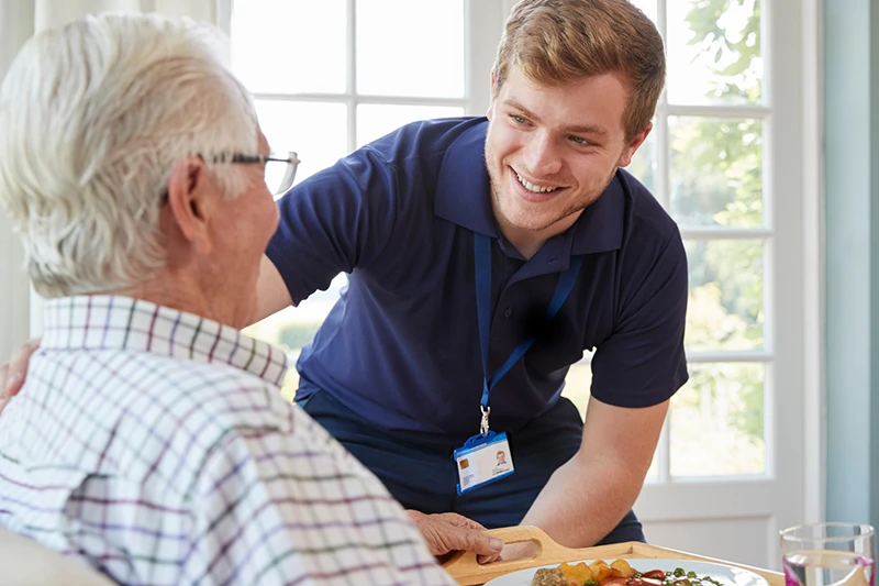 Care home staff member supporting an older resident during mealtime