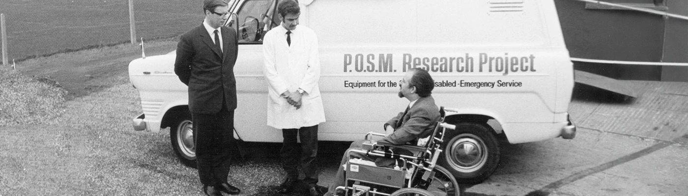 Historic photograph of the Possum Research Project team beside an accessibility support vehicle and wheelchair user