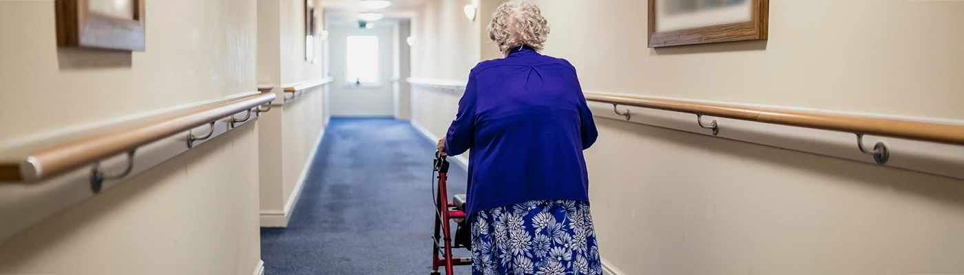 Walking with Purpose in Dementia Care Older woman using a rollator walking through a care home corridor, representing walking with purpose and dementia care support